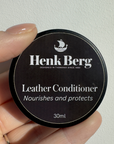 Henk Berg Leather Conditioner jar in hand, nourishes and protects vegetable-tanned leather, ideal for leather purses.